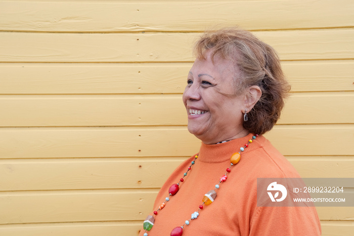 Portrait of smiling senior woman against yellow wall