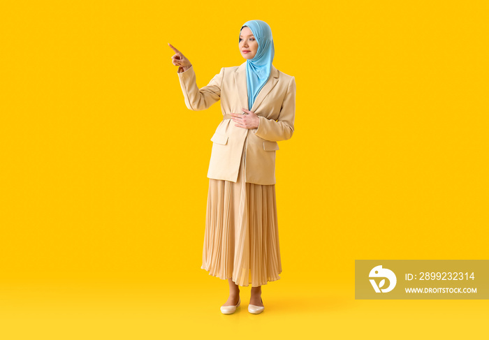 Pregnant Muslim woman pointing at something on color background