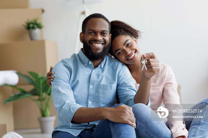 Glad cheerful young african american family show key and enjoy purchase of real estate in room with cardboard boxes