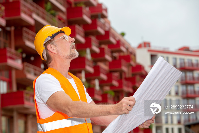 handsome worker in his 50s with helmet standing outside and holding a plan