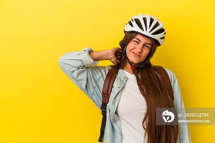 Young student caucasian woman wearing a bike helmet isolated on yellow background touching back of head, thinking and making a choice.