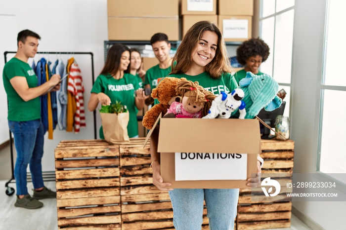 Group of young volunteers working at charity center. Woman smiling happy and holding box with toys to donate.