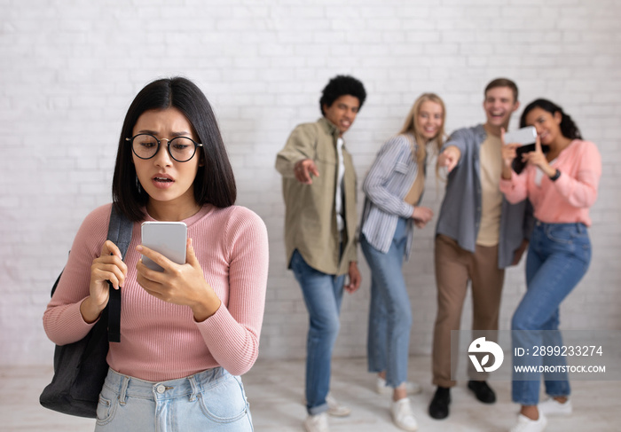 Humiliation, education and bullying. Sad asian young female in glasses looks at phone