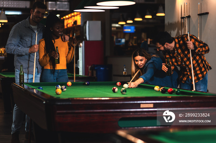 Four smiling friends in bar playing billiard together.