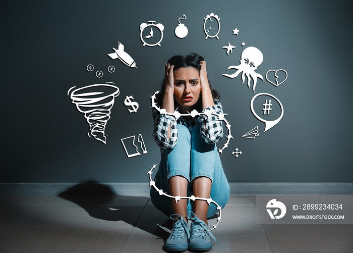 Depressed young woman sitting near dark wall