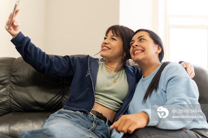 Two women sitting on sofa and using smartphone to take selfie