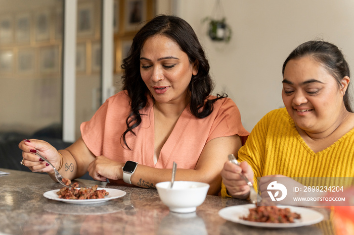 Mother eating dinner with down syndrome daughter at home