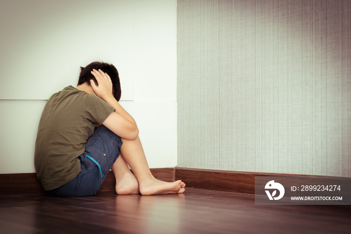 Young Asian preteen/teenage boy sitting alone at the corner of room, covering his ears, face down crying. Cyber Bullying, Teen problems, Loneliness, Traumatic, Stressed, frustrated and lost.