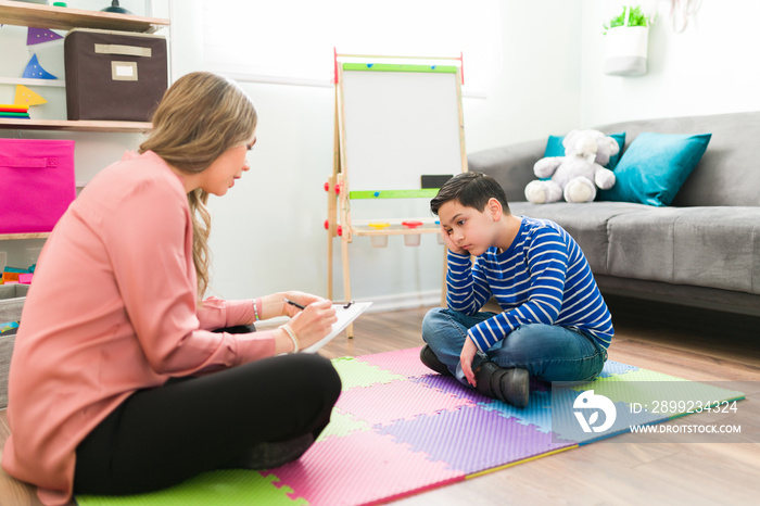 Depressed boy sitting on the floor with his child therapist