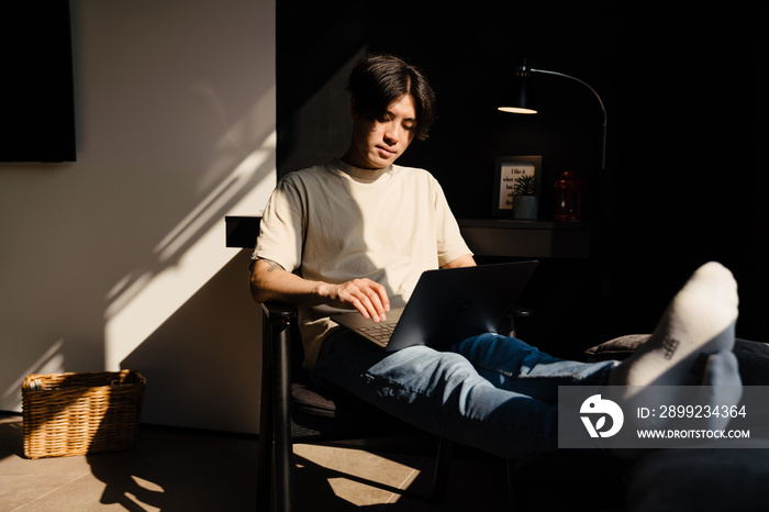 Asian young man sitting on chair and using laptop computer at home