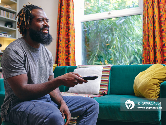 Man sitting on sofa, holding remote control