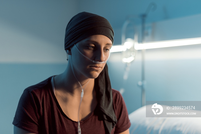 Sad young woman with cancer sitting on the hospital bed