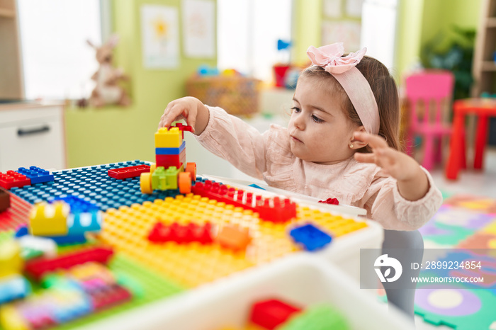 Adorable blonde toddler playing with construction blocks sitting on table at kindergarten