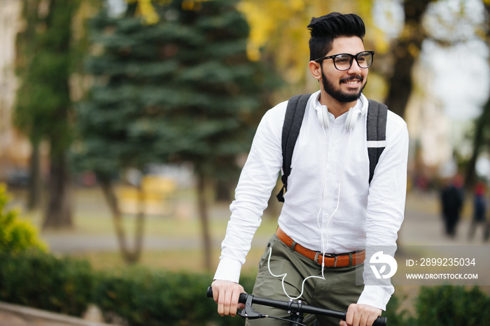 Indian stylish bearded student man with backpack with bicycle walking on street