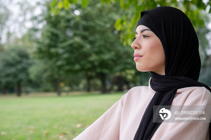 Portrait of woman in hijab and pink tracksuit meditating in park