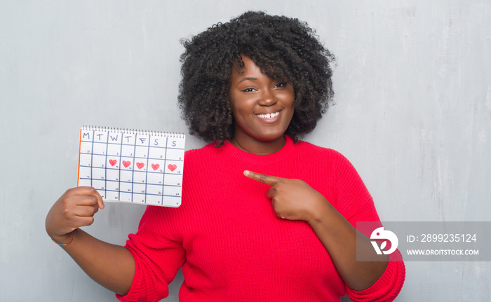 Young african american woman over grey grunge wall holding menstruation calendar very happy pointing with hand and finger