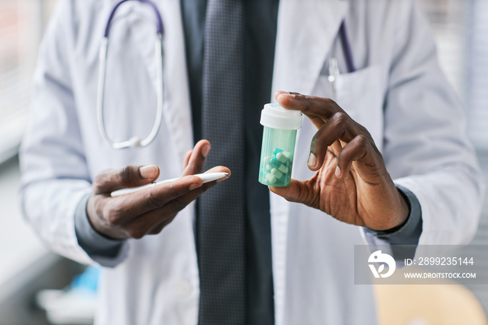 Close up black doctor pointing at bottle of pills explaining medication