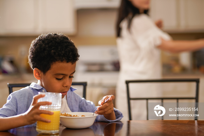 little boy eating cereal with mom in background