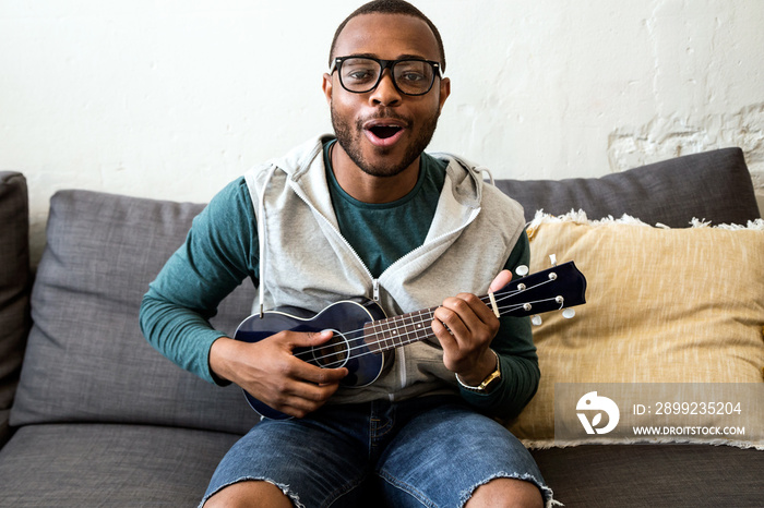 Handsome young black man playing the guitar at home.