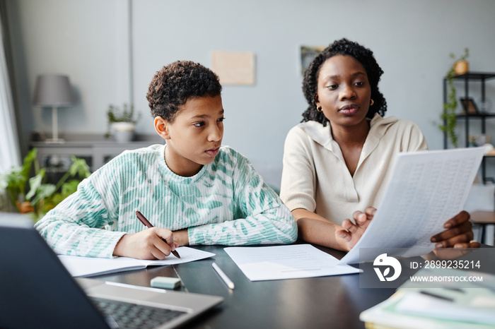 Portrait of black teenage girl studying at home with mother or tutor helping preparing for exam