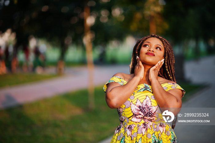 Cute small height african american girl with dreadlocks, wear at coloured yellow dress, posed at sunset.