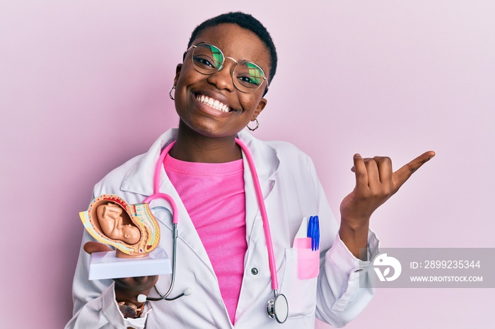 Young african american doctor woman holding anatomical model of female uterus with fetus smiling happy pointing with hand and finger to the side