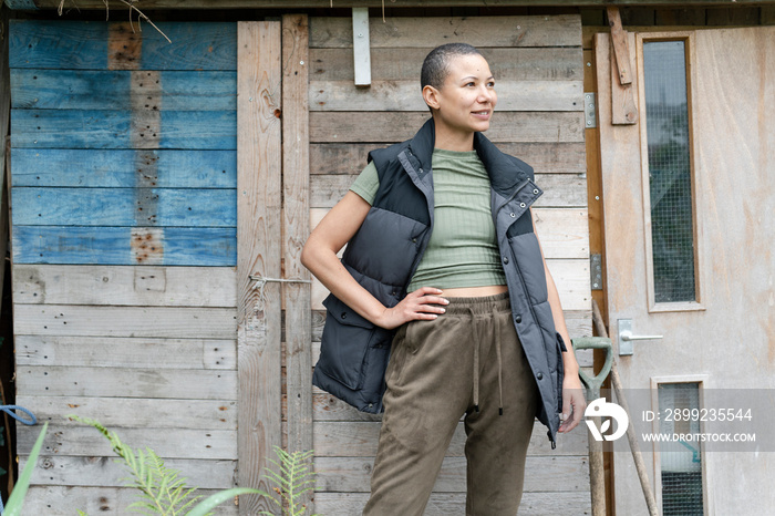 Portrait of smiling woman standing in front of hut in urban garden