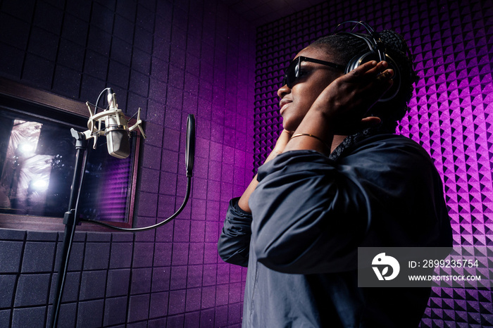 afro american woman with pigtails hairstyle headphones in a cap and a hood sunglasses recording hip hop song track.