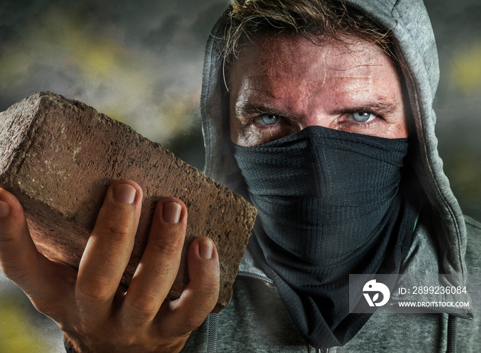 young man as ultra and radical anarchist rioter . furious antifa protester in face mask throwing brick hostile on street on demonstration in violet riot and chaos