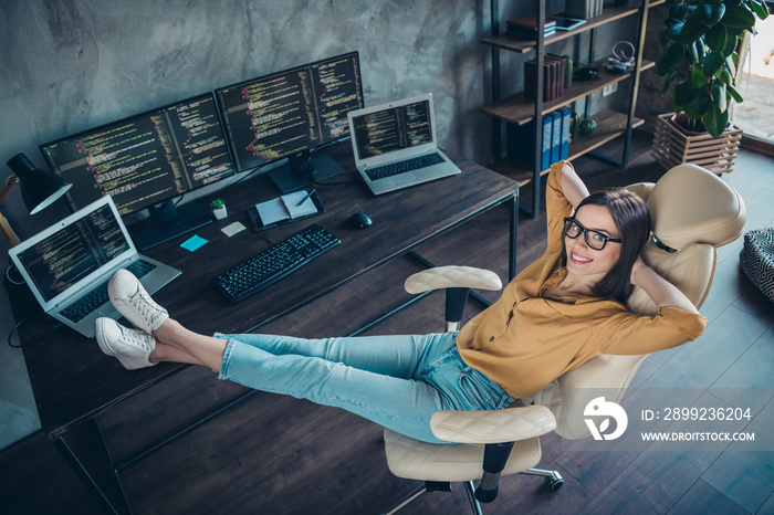 Full length body size view of attractive cheery girl geek hacker putting legs on table resting in chair at workplace workstation indoors