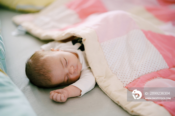 Baby sleeps on bed covered with pink patchwork quilt