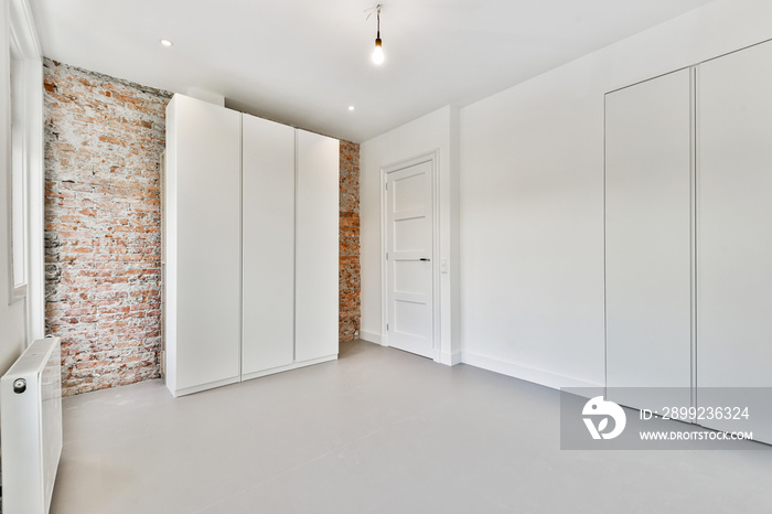 Interior of loft room with minimalist style wardrobe located near balcony doors and windows against brick wall in contemporary apartment