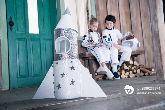 toy rocket and children astronauts behind using digital tablet