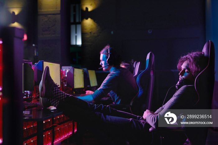 Young gamer relaxing on his chair in front of computer after computer game in dark room of computer club