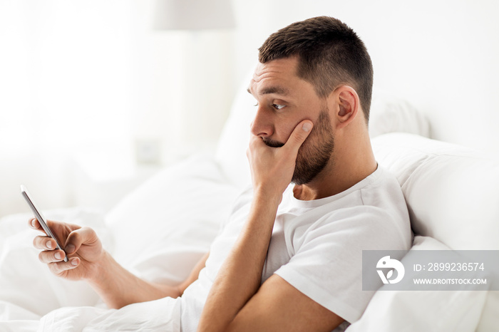 young man with smartphone in bed in morning