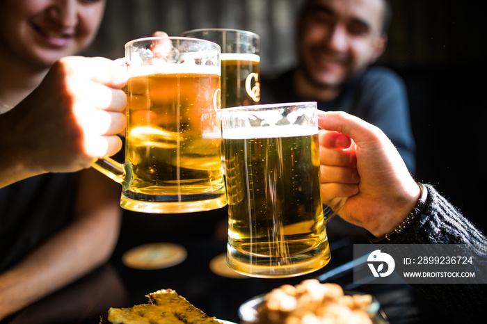 Close up of clanging glasses of beer of three friends in pub