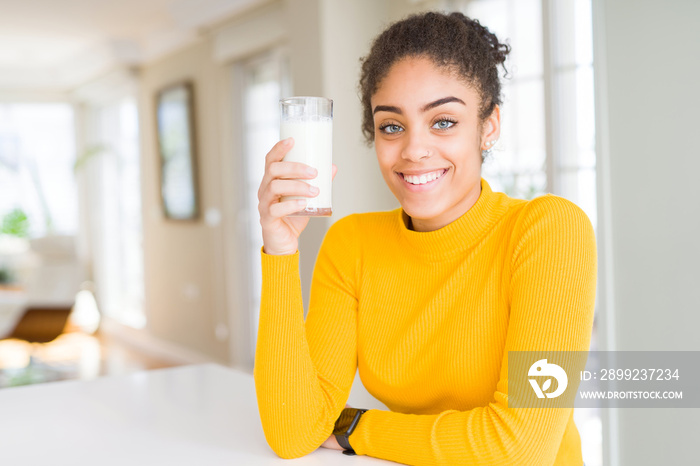 Young african american woman drinking a glass of fresh milk with a happy face standing and smiling with a confident smile showing teeth