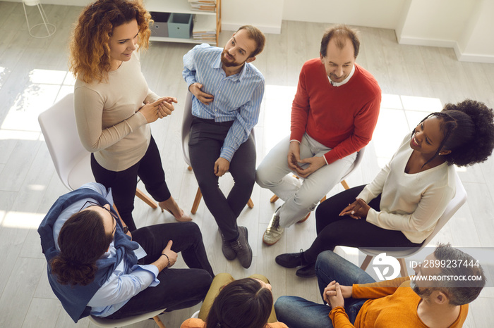 View from above of diverse people talking during meeting with professional psychologist or therapist. High angle shot of young woman telling her story to supportive patients in group therapy session