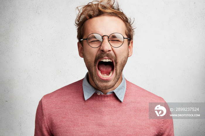 Emotional mad crazy young male screams loudly and with anger, being stressed and in panic, frowns face, isolated over white concrete wall. Negative human emotions, feelings, reaction concept