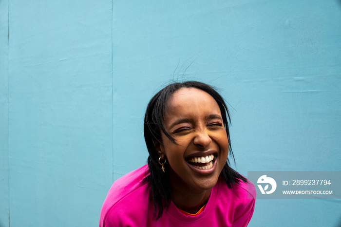 Young woman in pink sweatshirt laughing outdoors