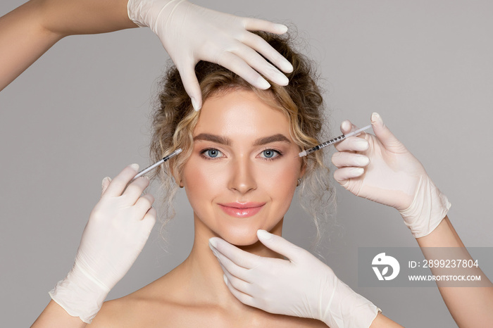 Attractive young woman getting injection for eyes area by two cosmetologists giving anti aging serum shot on female face