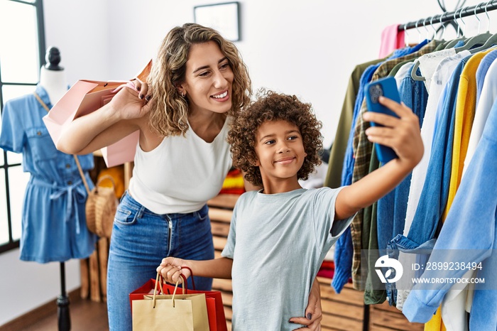 Mother and son smiling confident holding shopping bags make selfie by the smartphone at clothing store