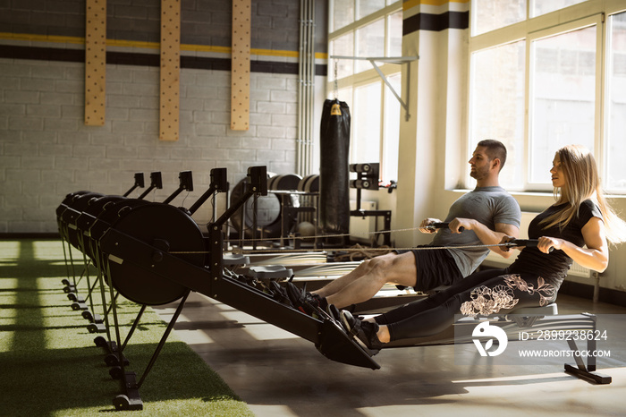 Man and woman training on rowing machines in gym together