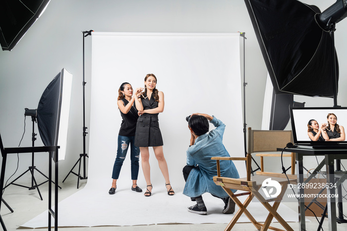 behind the scene of Professional photo shooting at the studio: a beautiful young asian model is smiling and posing with makeup artist is makeup photographer is taking pictures with a digital camera