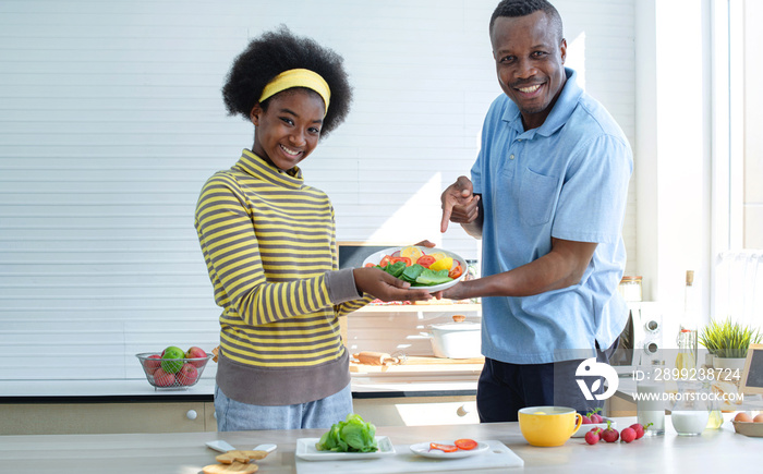 African father and daughter showing their salad plate which they are made together in kitchen, close up