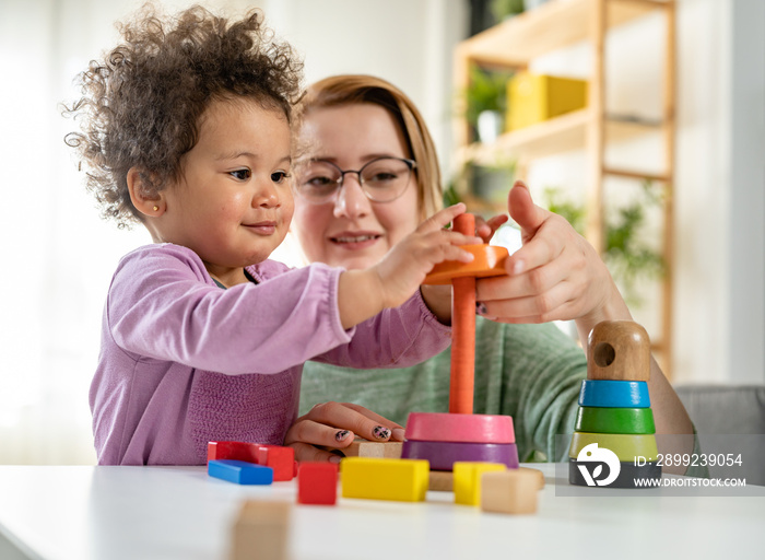 Mother looking at a child playing with an educational didactic toy. Young woman and child playing with didactic toys