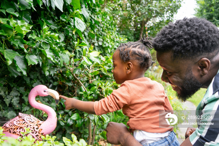 Father and daughter (2-3) looking at flamingo sculpture in garden