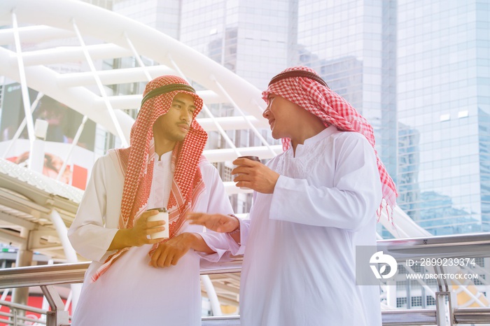 Two young Arabian businessman are having drink and friendly conversation on modern white building background