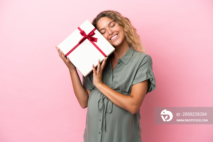 Girl with curly hair isolated on pink background pregnant and holding a gift