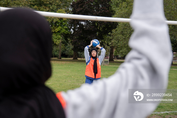 Two women in hijabs playing soccer in park